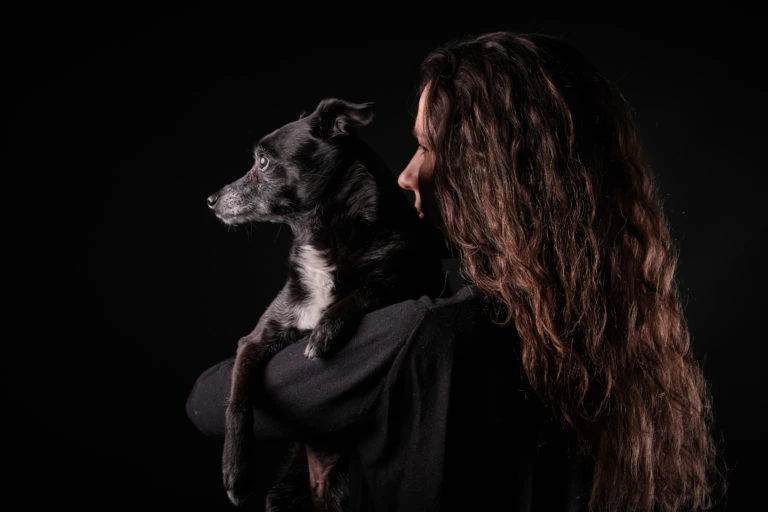 Mujer sosteniendo a un perro blanco y negro sobre fondo oscuro