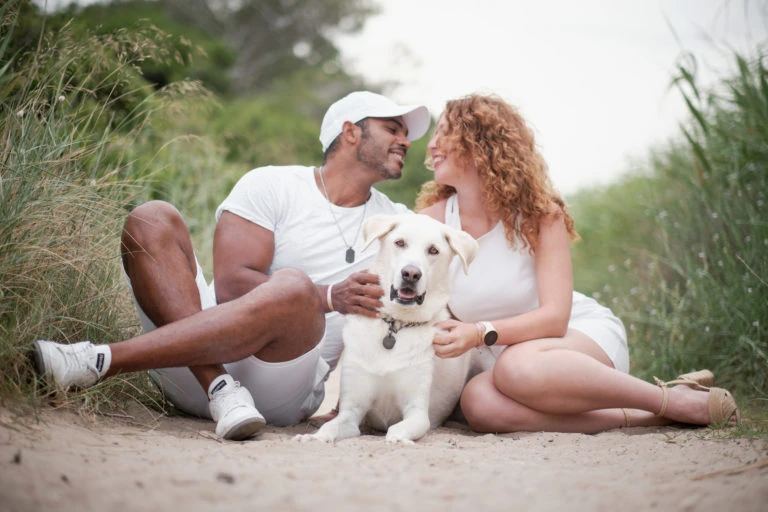 Pareja sentada con su perro blanco en un camino al aire libre