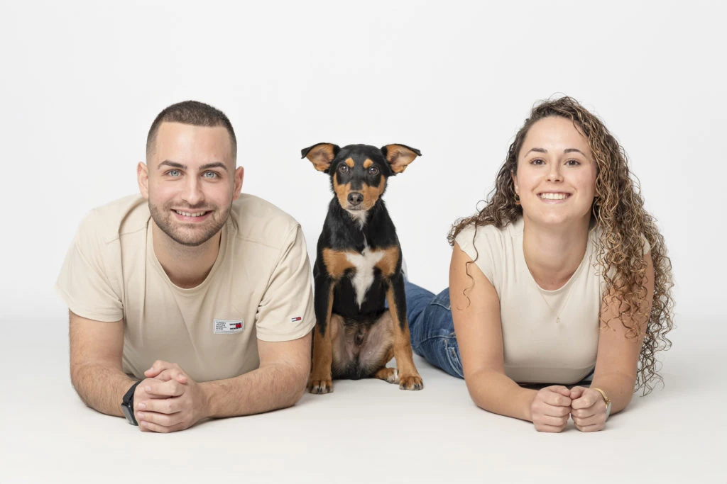 Pareja tumbada junto a su perro sobre fondo blanco