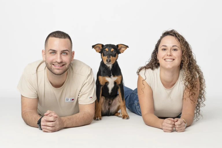 Pareja tumbada junto a su perro sobre fondo blanco