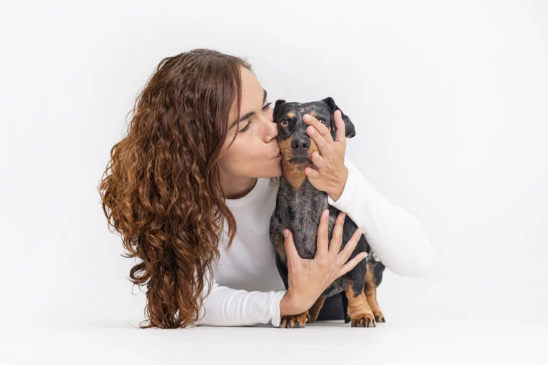 Mujer besando a su perro pequeño sobre fondo blanco