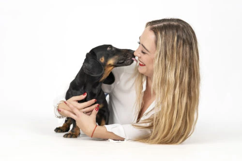 Mujer junto a un perro pequeño sobre fondo blanco