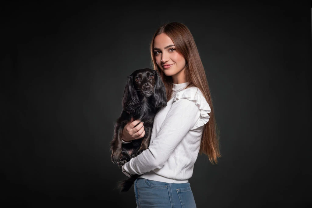 Mujer sosteniendo a su perro negro sobre fondo oscuro