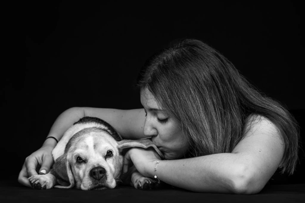 Mujer acariciando a su perro tumbado, en blanco y negro